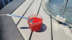 Strawberry rhubarb jam with a spoon sticking in the jar, sitting on a fire table outside