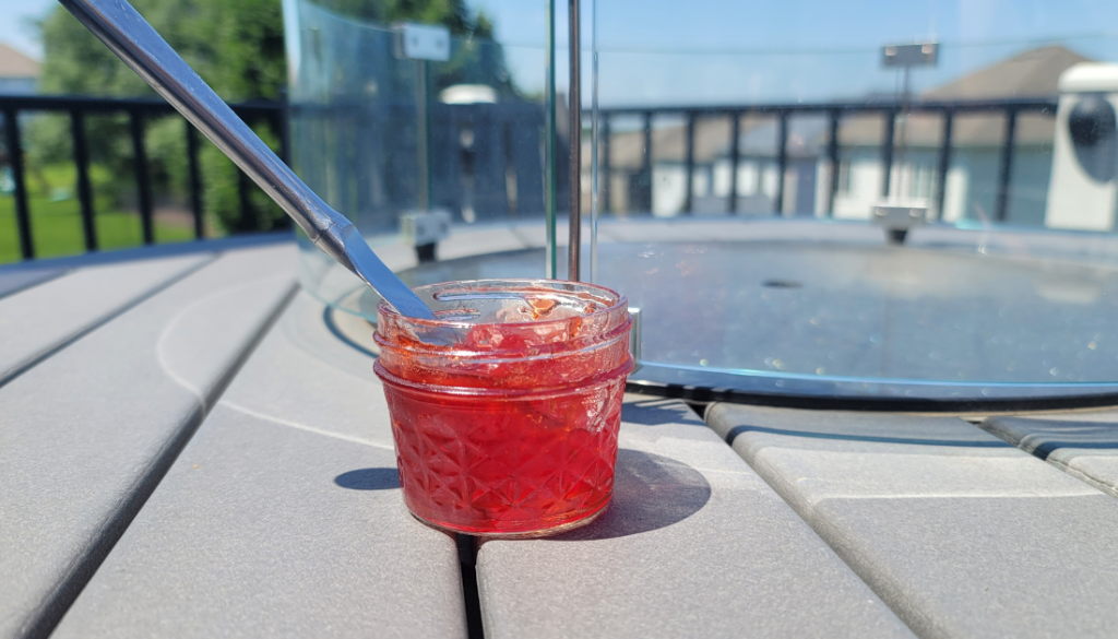 Strawberry jam - jar of jam on a table outside with a knife sticking into the jar