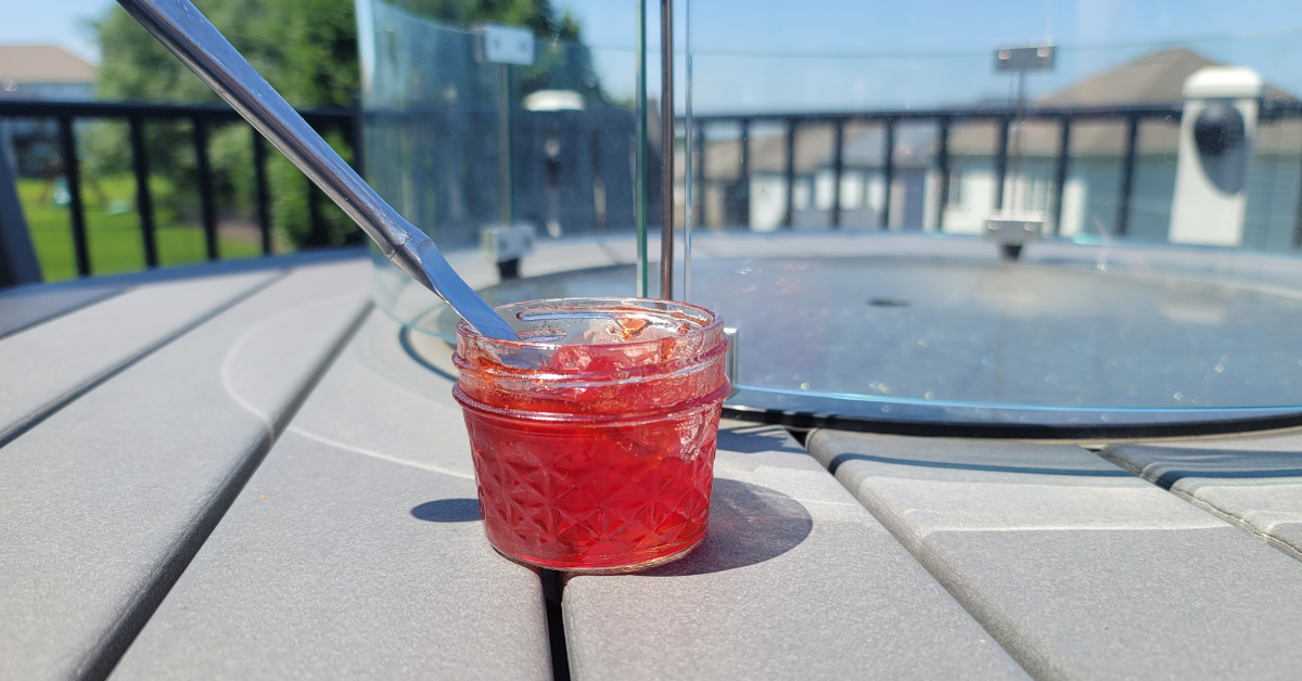 Strawberry jam - jar of jam on a table outside with a knife sticking into the jar